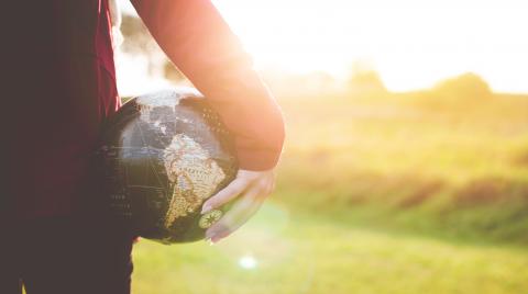 Person Holding a Globe to their side while sunshines in the background