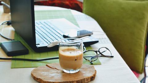 Coffee sitting next to a laptop on a desk with a green chair in the background.