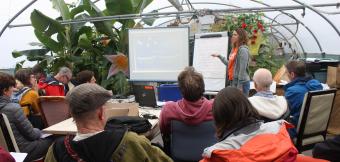 Students gather around a presentation with plants in the background