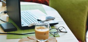 Coffee sitting next to a laptop on a desk with a green chair in the background.