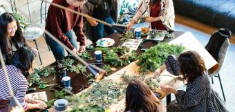 Six people are gathered around a table working on crafts