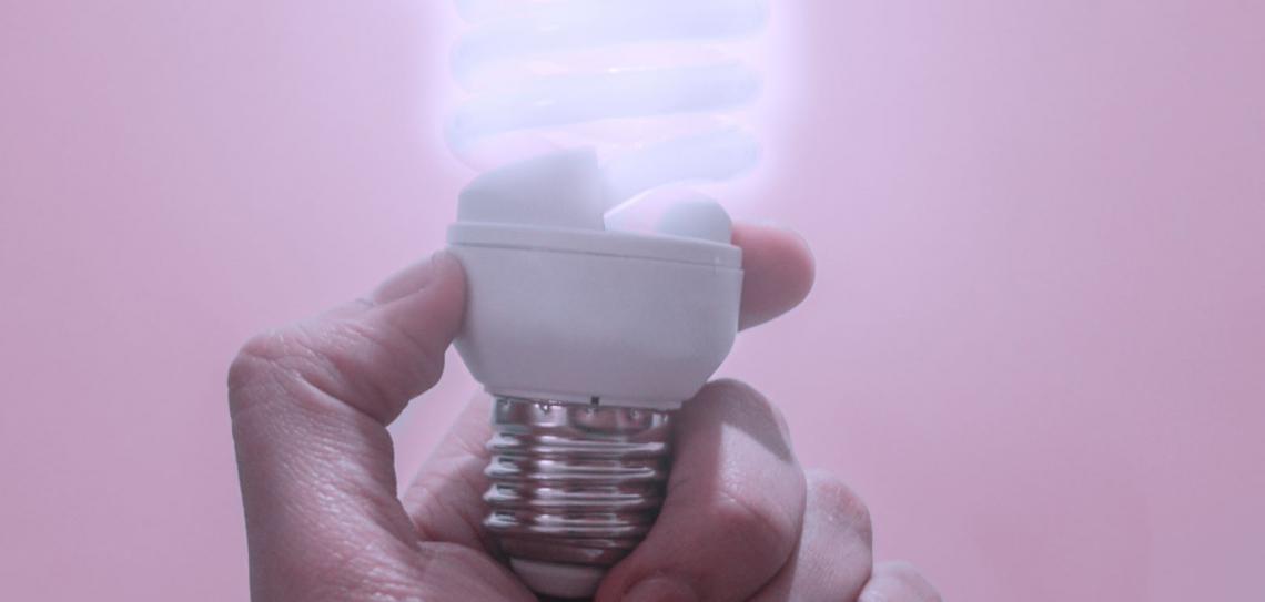 A hand holds up a lit low energy bulb.