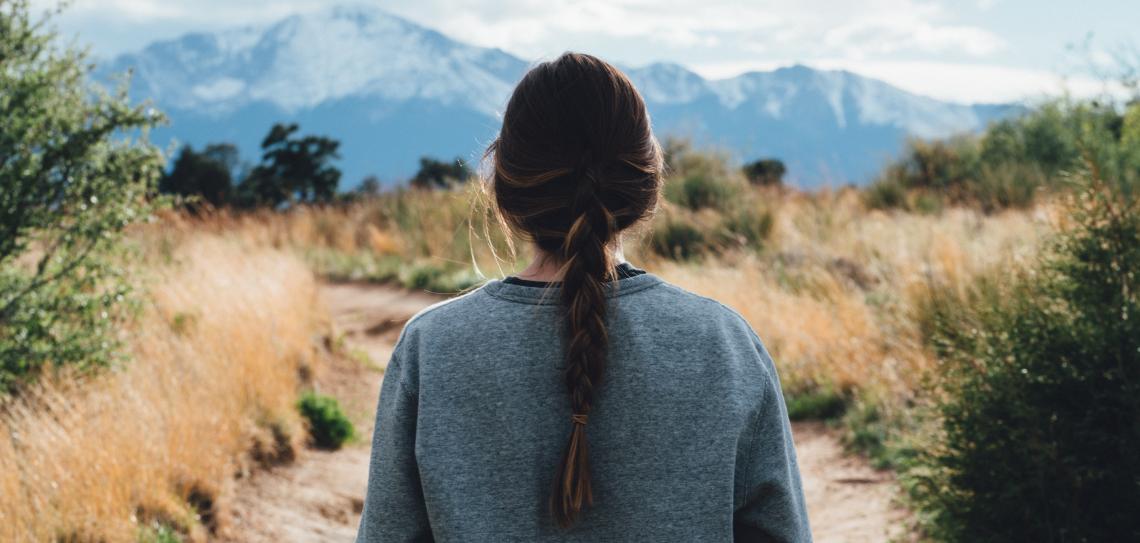 Woman facing a trail with moutains in the background