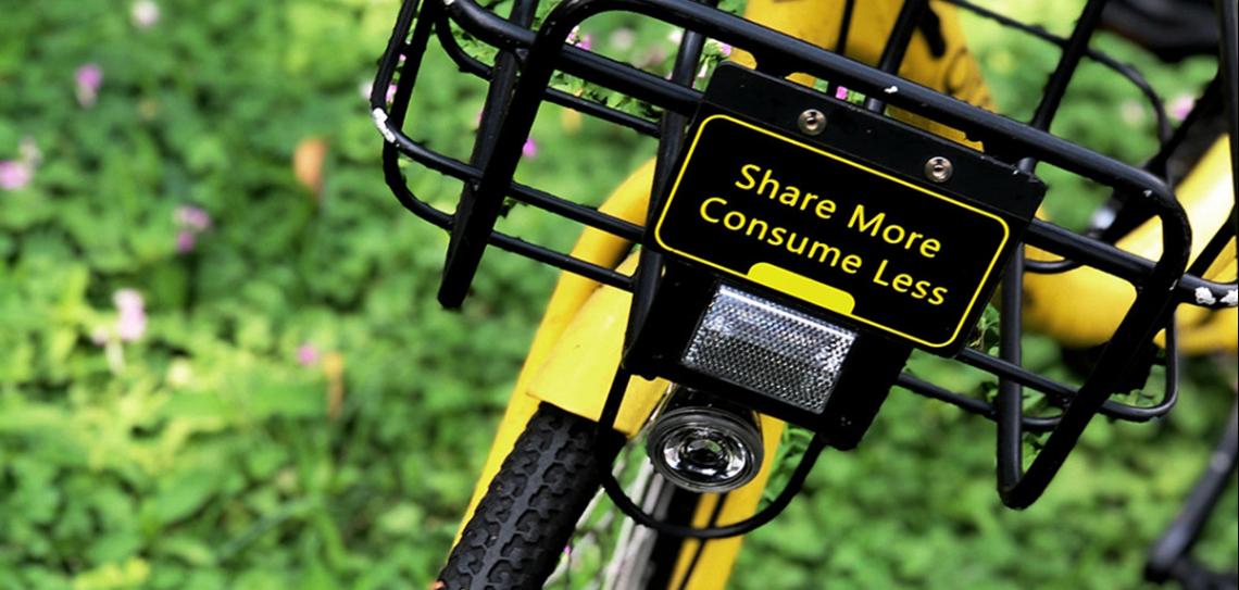 Yellow bike on green grass with a sign that says 'Share more, consume less'