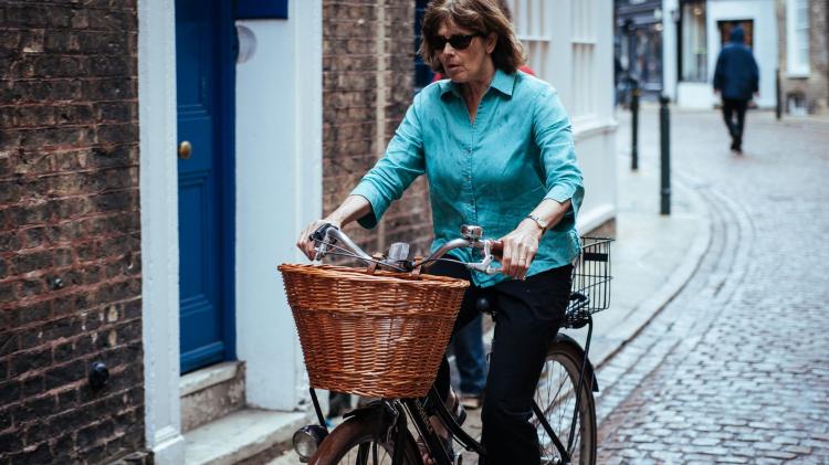 A middle aged woman rides a bike on a cobbled street