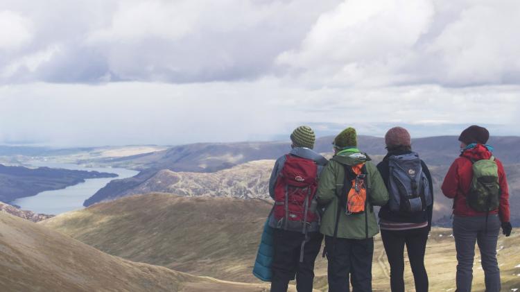 4 women on a hilltop enjoying the view of a lake. 