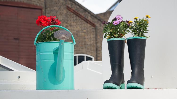 Watering can and old boots full of flowers on a white balcony