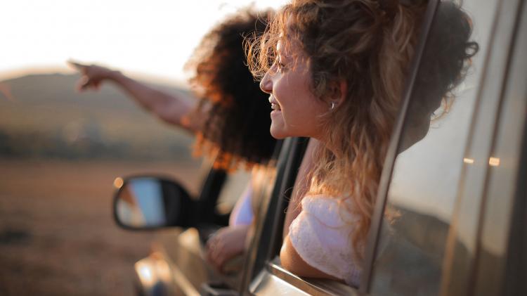 Two women lean out a car window on a roadtrip