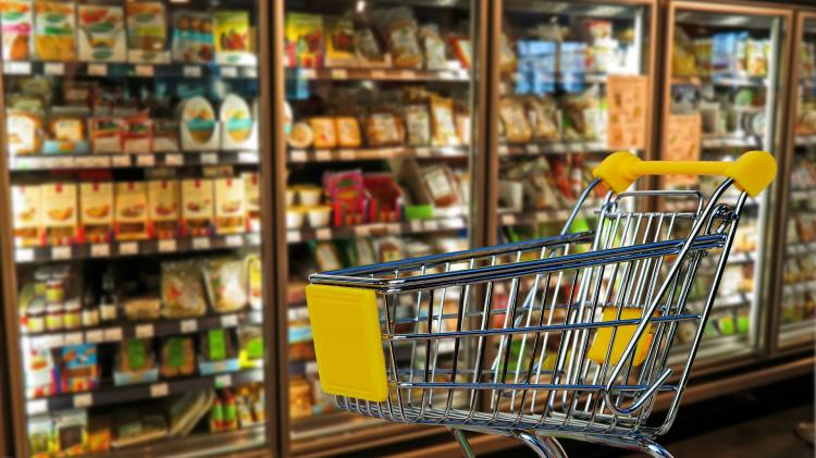 Grocery Cart in front of a cold food section of a grocery store.