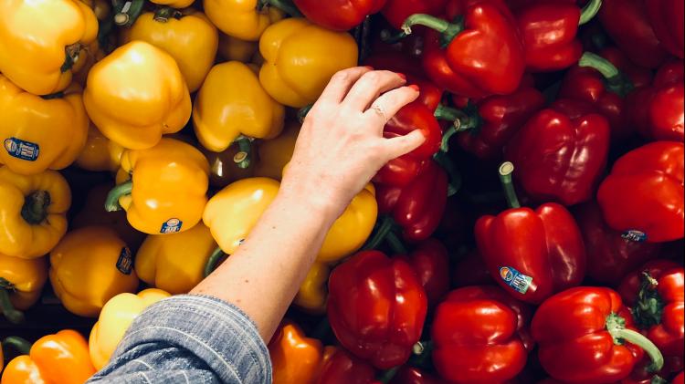 Hand reaching out to choose between and red and yellow pepper