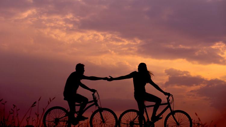 Climate change gives us all a chance to see life differently, like treasuring relationships more than possessions. Photo: Everton Vila - Unsplash.com Two people on bikes riding bikes with a orange and pink sunset in the background