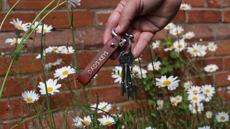 Person holding set of keys with flowers in the back ground