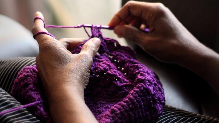 Learning a new skill is a simple way to buy less and make more. Photo: Imani - unsplash.com Hands knitting a purple hat